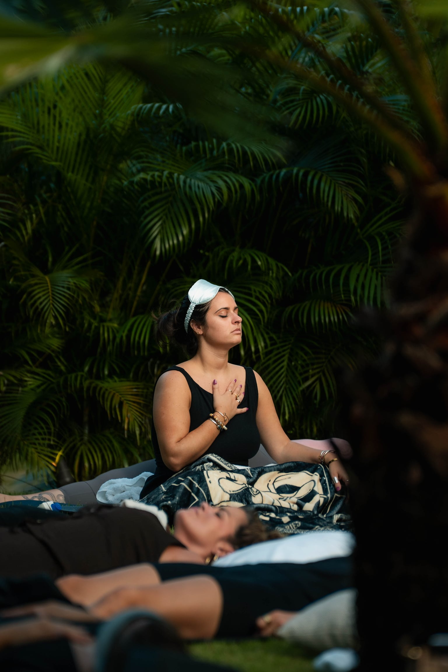 A guest seated among the palms, eyes closed, hand on her heart